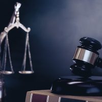 A gavel on a book with a blurred statue of Lady Justice in the background.